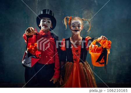 Trick or treat. Boy and girl, children wearing costumes for halloween, standing with basket for candies against dark vintage background 106210165