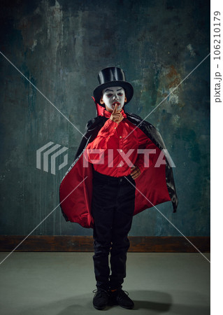 Shh. Keeping secret. LLittle boy, child in image of creepy vampire wearing costume and makeup against vintage green background 106210179