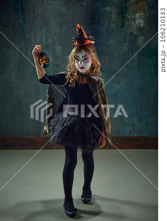 Little girl, child in image of witch, with creepy makeup and costume standing against dark vintage background. Spooky season Little girl, child in image of witch, with creepy makeup and costume standing against dark vintage background. Spooky season 106210183