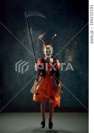 Girl, child in costume and makeup for halloween party jumping with frightening face against dark vintage background 106210191