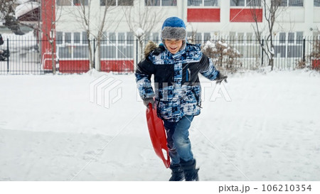 Boy happily running with plastic sleds in the snow, enjoying the fresh air and winter scenery. Boy happily running with plastic sleds in the snow, enjoying the fresh air and winter scenery. 106210354