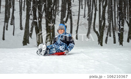Young boy sledging down a snowy hill with excitement and exhilaration. The perfect scene to showcase the fun and joy of winter playtime during the holiday season. Young boy sledging down a snowy hill with excitement and exhilaration. The perfect scene to showcase the fun and joy of winter playtime during the holiday season. 106210367