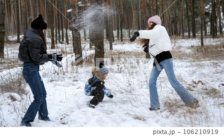 Two teenage girls playing with little boy in snow and throwing snowballs. People playing outdoors, winter holidays and vacation, active leisure. Two teenage girls playing with little boy in snow and throwing snowballs. People playing outdoors, winter holidays and vacation, active leisure. 106210919