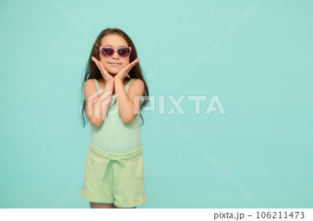 Lovely little girl holding her face with her hands, looking at camera, isolated on blue studio background. Copy ad space Lovely little girl holding her face with her hands, looking at camera, isolated on blue studio background. Copy ad space 106211473