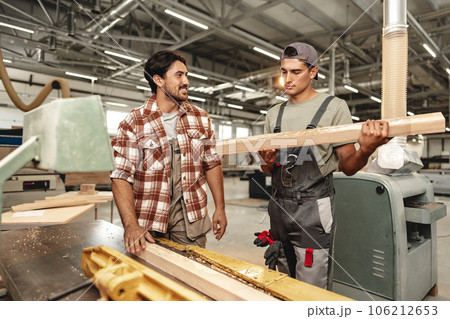 Two young carpenters working with wood standing at table in workshop 106212653