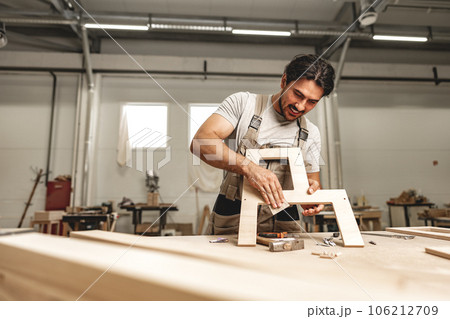 Young man carpenter wearing uniform working in joinery making wooden furniture 106212709