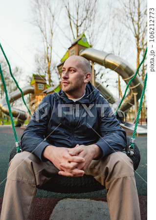 Smiling bald man sitting on a swing in a playground 106212773