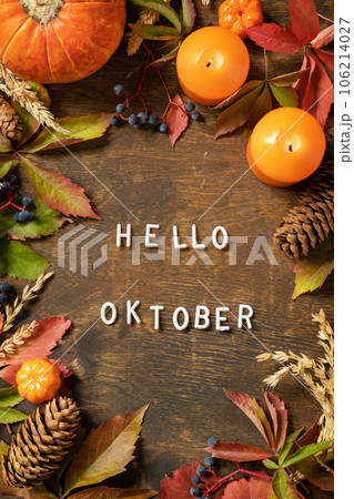 Hello oktober text, autumn season. Greeting card, fallen leaves, pumpkins and cones on a wooden board. Autumn natural background. View from above. 106214027