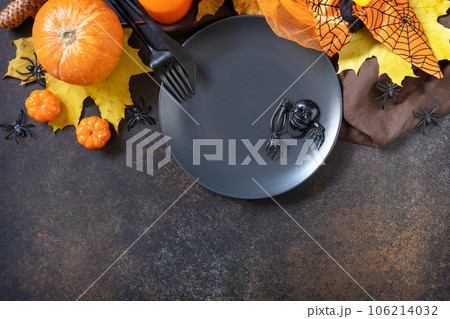 Halloween table setting. Blank black plate with decoration pumpkins, autumn leaves, spiders on a stone background. Card or menu template. Top view. Copy space. 106214032