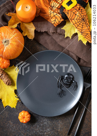 Halloween table setting. Blank black plate with decoration pumpkins, autumn leaves, spiders on a stone background. Card or menu template. Top view. 106214033