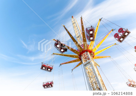 Scenic bottom view high chain swing flying carousel against blue sky. Merry go round roundabout chairoplane at portable amusement park. People enjoy having family fun play riding at fair festival 106214808