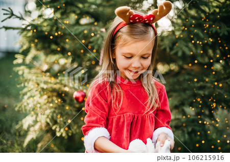 Christmas in july. Child waiting for Christmas in wood in summer. portrait of little girl in red dress decorating christmas tree. winter holidays and people concept. Merry Christmas and Happy Holidays Christmas in july. Child waiting for Christmas in wood in summer. portrait of little girl in red dress decorating christmas tree. winter holidays and people concept. Merry Christmas and Happy Holidays 106215916
