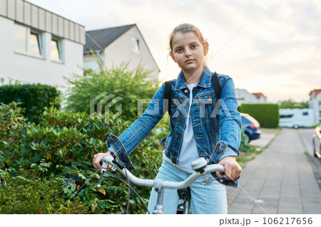 Schoolgirl child 10, 11 years old with backpack on bicycle on street near house Schoolgirl child 10, 11 years old with backpack on bicycle on street near house 106217656