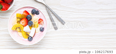 Healthy breakfast or dessert yogurt bowl with fresh banana, strawberry, blueberry, cocos, kiwi top view, rustic wooden white background with spoon. Copy space Healthy breakfast or dessert yogurt bowl with fresh banana, strawberry, blueberry, cocos, kiwi top view, rustic wooden white background with spoon. Copy space 106217693