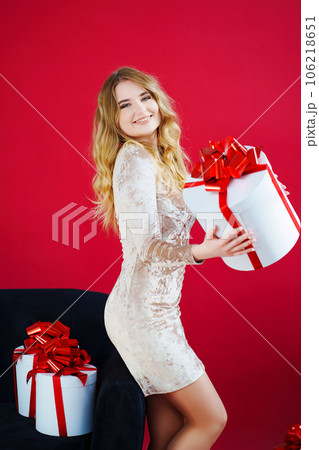 a beautiful woman in an elegant dress with a gift in the red room by the sofa a beautiful woman in an elegant dress with a gift in the red room by the sofa 106218651