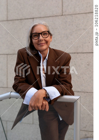 portrait of a model of a slender gray-haired woman of mature years dressed in an elegant brown suit 106218820