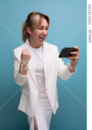 pretty young fair-haired business woman in a jacket and dress joyfully watches a video on the phone 106219109