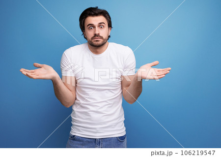 bearded brunette guy in white t-shirt shows refusal gesture on studio background with copy space 106219547