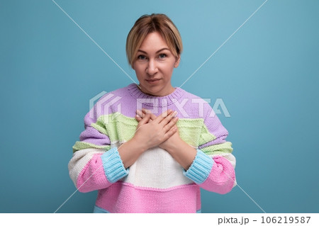 smiling blond young woman in a bright jacket thanks from the bottom of her heart on a blue 106219587