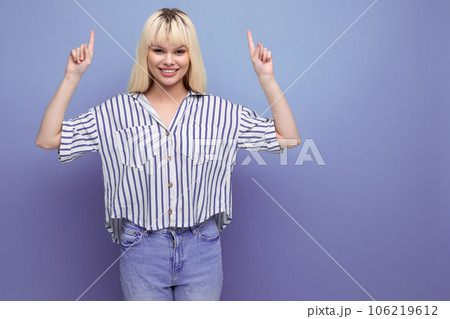 smiling positive blond young woman in striped shirt pointing finger at advertisement on studio 106219612