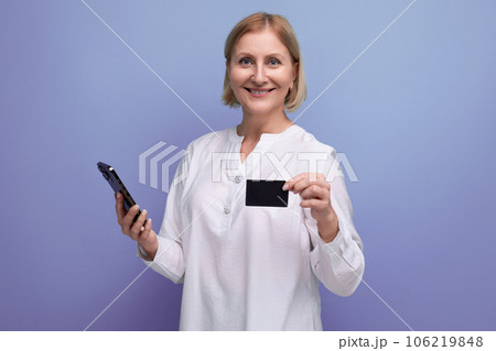 confident slim blonde mature woman in white blouse holding plastic card for shopping with mockup 106219848