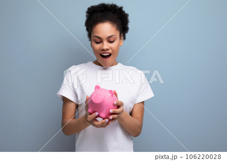young happy hispanic brunette woman saving money for a dream in a pink piggy bank 106220028