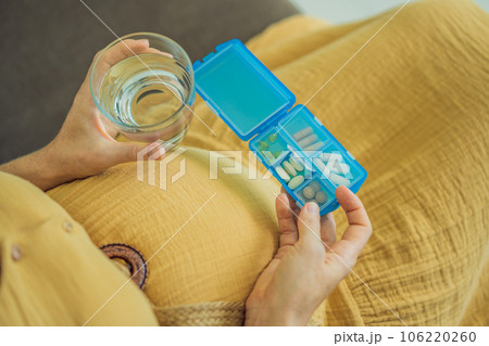Prenatal Vitamins. Portrait Of Beautiful Smiling Pregnant Woman Holding Pill Box and a glass of water, Taking Supplements For Healthy Pregnancy While Sitting On Couch At Home, Free Space Prenatal Vitamins. Portrait Of Beautiful Smiling Pregnant Woman Holding Pill Box and a glass of water, Taking Supplements For Healthy Pregnancy While Sitting On Couch At Home, Free Space 106220260