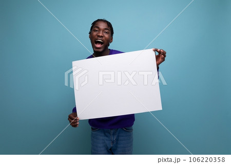 american young man in a blue sweatshirt holding a paper poster with a mockup 106220358
