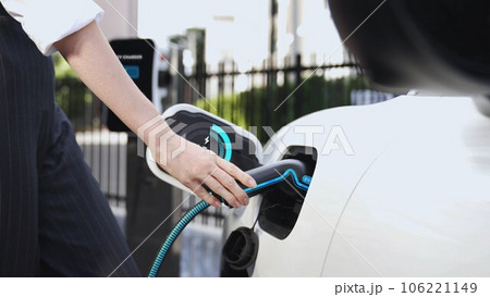 Businesswoman recharge her electric car from charging station. Peruse Businesswoman recharge her electric car from charging station. Peruse 106221149