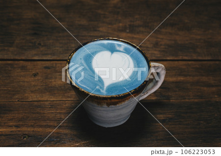 Close-up of a cup of Blue latte on wooden table. The vibrant blue colour of the drink is natural, Made from micro-milled Butterfly Pea Flower, which originated in Thailand. Close-up of a cup of Blue latte on wooden table. The vibrant blue colour of the drink is natural, Made from micro-milled Butterfly Pea Flower, which originated in Thailand. 106223053