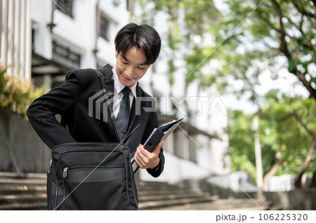 A happy Asian businessman finds his phone in his briefcase while walking down the stairs A happy Asian businessman finds his phone in his briefcase while walking down the stairs 106225320
