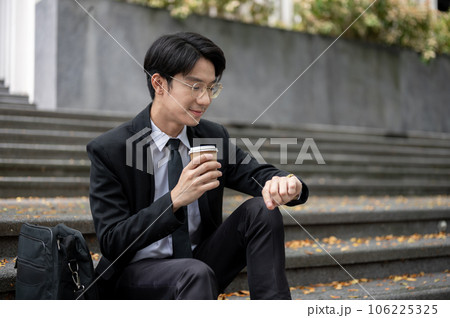 A businessman is sipping coffee and checking time on his watch while sitting on a staircase 106225325