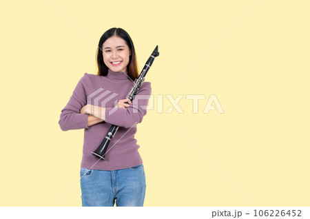 An attractive Asian woman holding a clarinet, stands against an isolated yellow background. 106226452