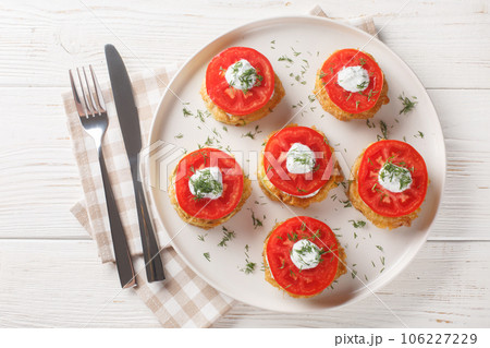 Homemade fried zucchini in egg batter served with creamy garlic sauce, dill and fresh tomatoes close-up in a plate. Horizontal top view 106227229