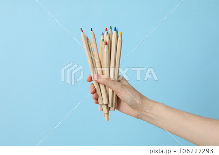 A female hand holds multi-colored pencils on a blue background 106227293