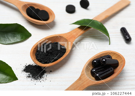 Activated charcoal tablets with wooden spoon and leaves 106227444