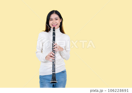 A smiling Asian female musician with a clarinet stands against an isolated yellow background 106228691