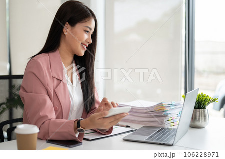 A beautiful Asian businesswoman or female accountant using a calculator at her desk A beautiful Asian businesswoman or female accountant using a calculator at her desk 106228971