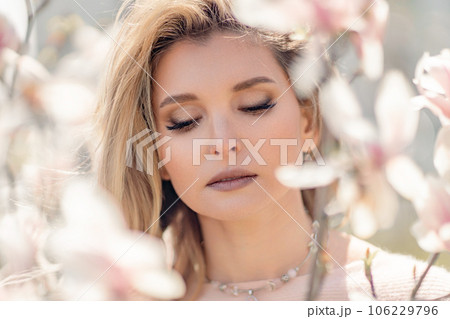 Portrait of a beautiful happy middle aged woman enjoying the smell in a blooming spring garden. Beautiful magnolia bushes, large flowers. Portrait of a beautiful happy middle aged woman enjoying the smell in a blooming spring garden. Beautiful magnolia bushes, large flowers. 106229796