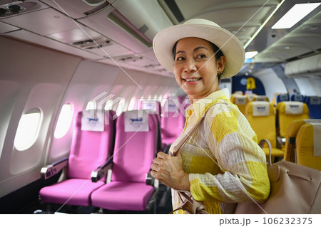 Smiling middle age female tourist with bag walking the aisle on plane. Retirement, travel and summer vacation concept 106232375