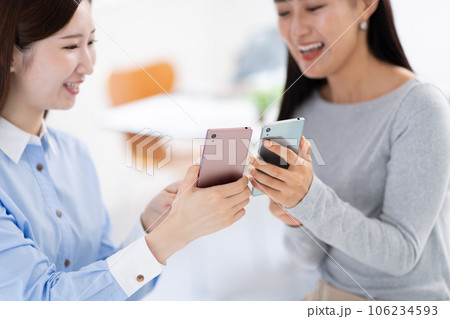 スマホを見せ合う女性・手元 106234593