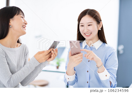 スマホを見せ合う女性・手元 106234596
