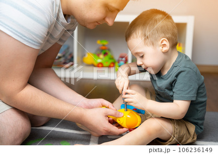 A little toddler boy 2,5 years is playing with a toy helicopter, assembling and disassembling it with father. Educational toys for kids. Children's room in home. Indoors 106236149