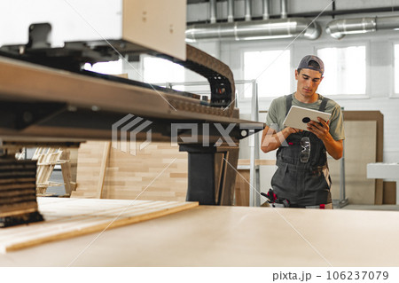 Young carpenter operating machine for wood processing at a furniture factory Young carpenter operating machine for wood processing at a furniture factory 106237079