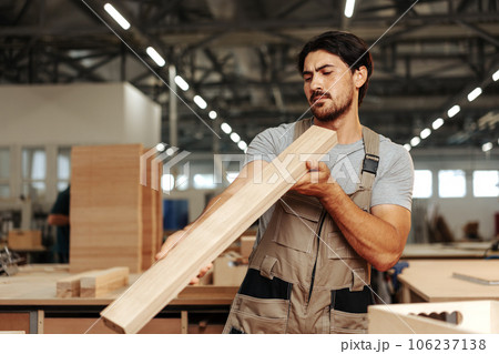 Young carpenter man looking and choosing wood plank at workshop in carpenter wood factory 106237138