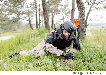 A man in a military uniform and a bulletproof vest works in the forest to demine the territory. A man warns of danger by making a red mark 106237576