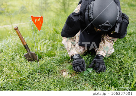 A man in a military uniform and a bulletproof vest works in the forest to demine the territory. A man warns of danger by making a red mark 106237601