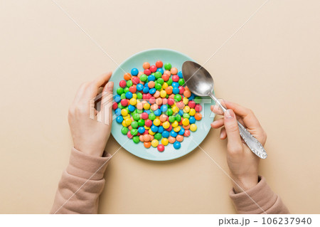 the girl holds cutlery in her hands and eats sweets in a plate. Health and obesity concept, top view on colored background 106237940