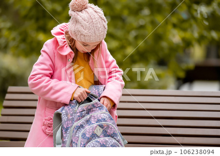 School girl kid looking at backpack sitting on the banch at autumn park. Beautiful female child resting after lessons 106238094