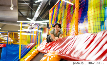 Pretty girl lying on colorful trampoline at playground park and smiling. Beautiful teenager during active entertaiments 106238125